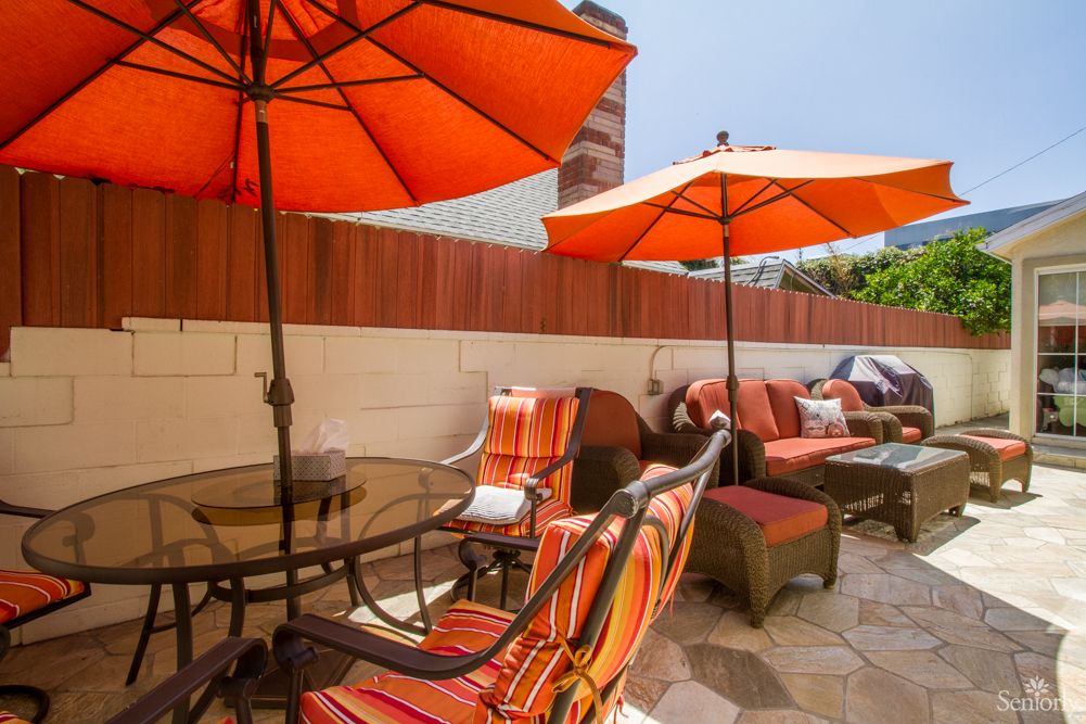 A cozy patio area with orange umbrellas, cushioned chairs, and a table set for outdoor relaxation.