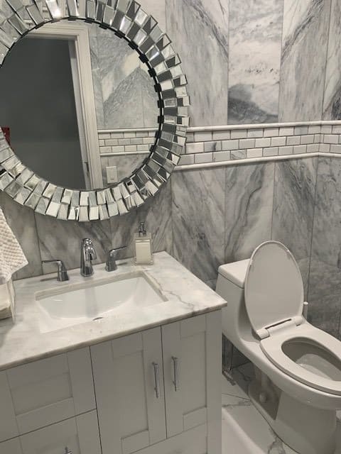 A modern bathroom with a marble sink countertop and decorative circular mirror.