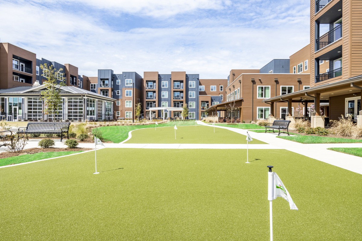 A modern residential building with a well-maintained outdoor lawn and golf putting green under a clear blue sky.