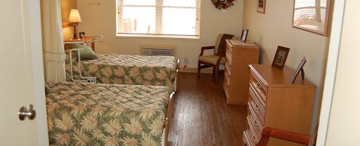A cozy bedroom featuring two twin beds with floral bedding, a wooden floor, and bright natural light coming from the window.