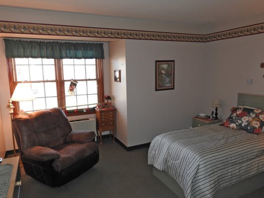 A neatly arranged bedroom with a bed, chair, and window.