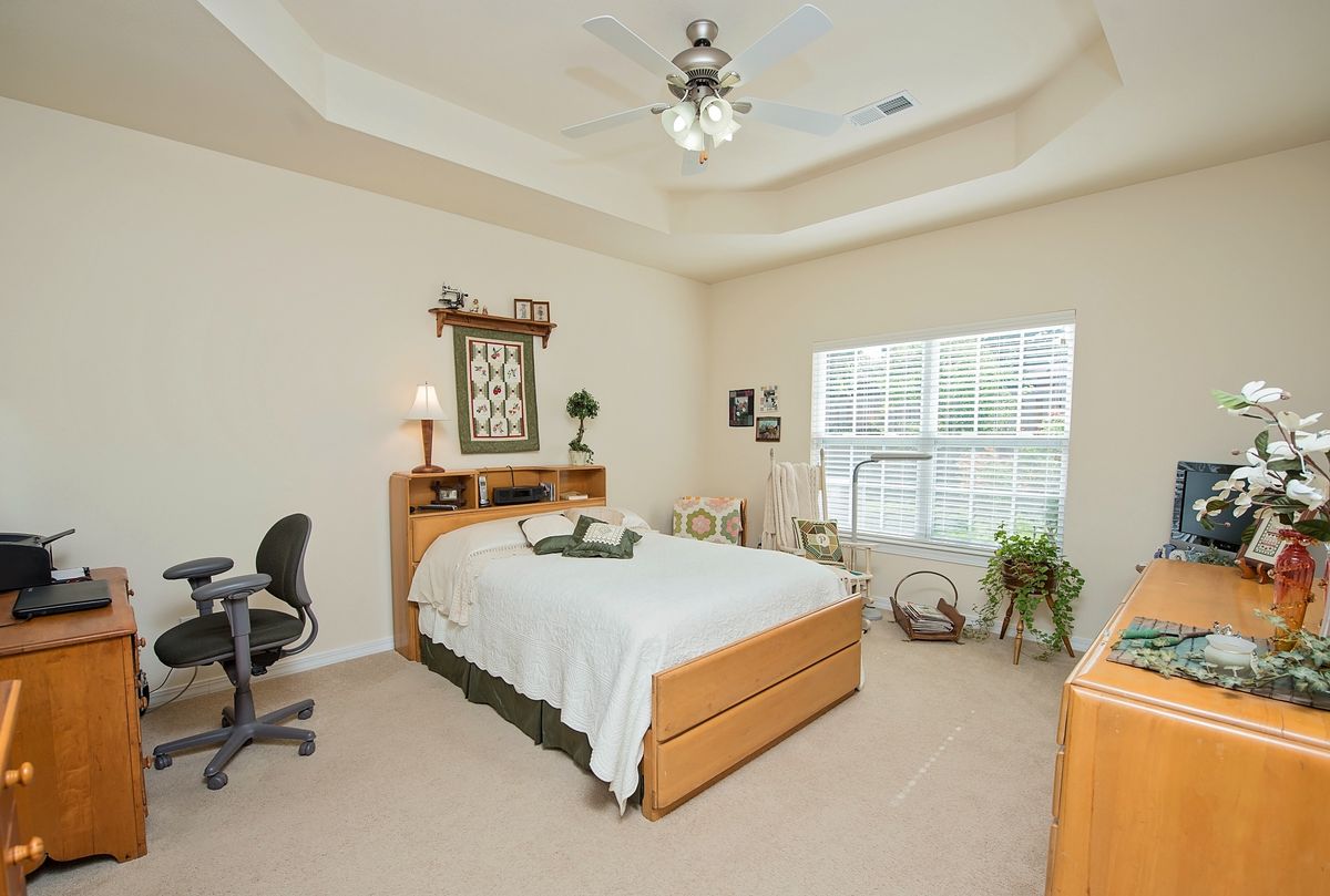 A modern bedroom with a neatly made bed, desk area, and elegant decor, bathed in natural light from a large window.