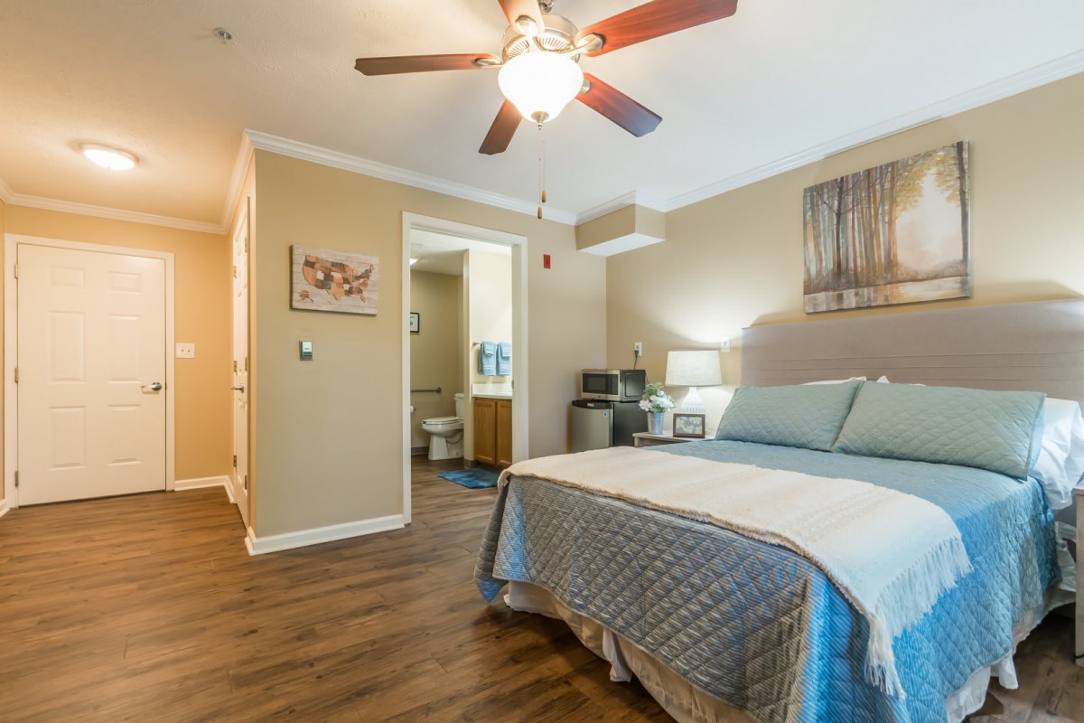 A cozy bedroom interior featuring a bed with blue bedding, a ceiling fan, and warm lighting.