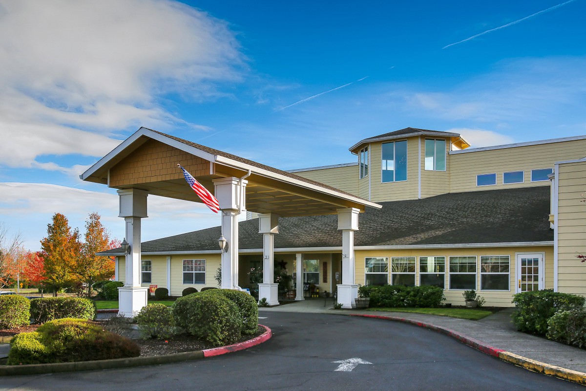 A welcoming building entrance with a flag and landscaped surroundings under a clear blue sky.