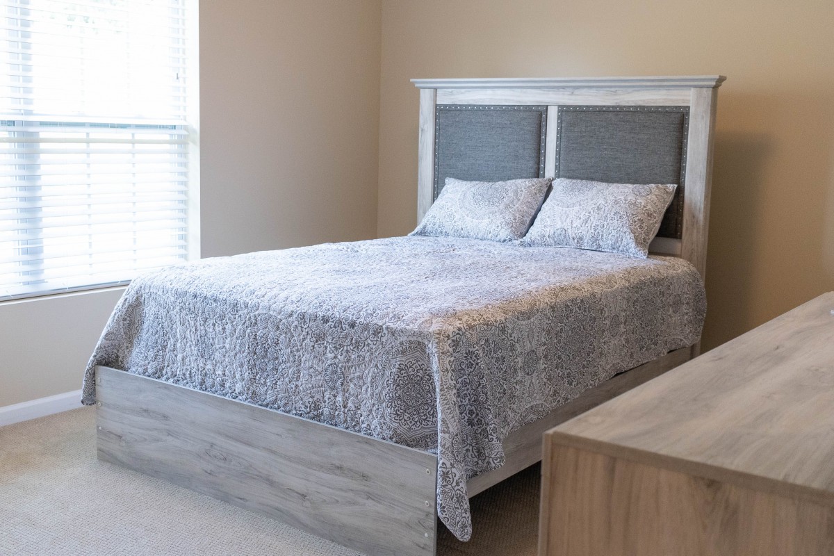 A minimalist bedroom with a neatly made bed and a light quilt.