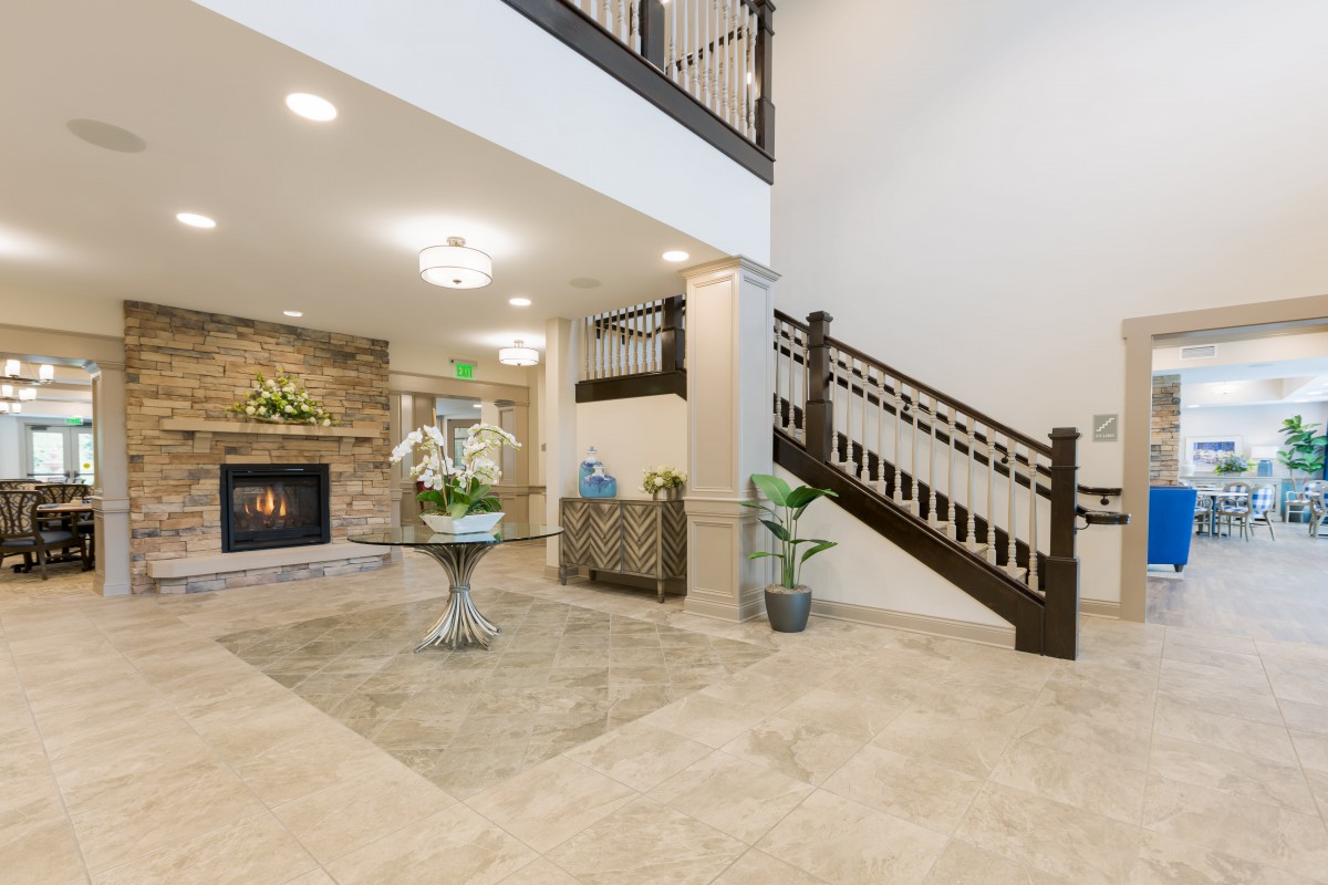 A modern foyer featuring a fireplace and a grand staircase, with decorative elements and indoor plants.