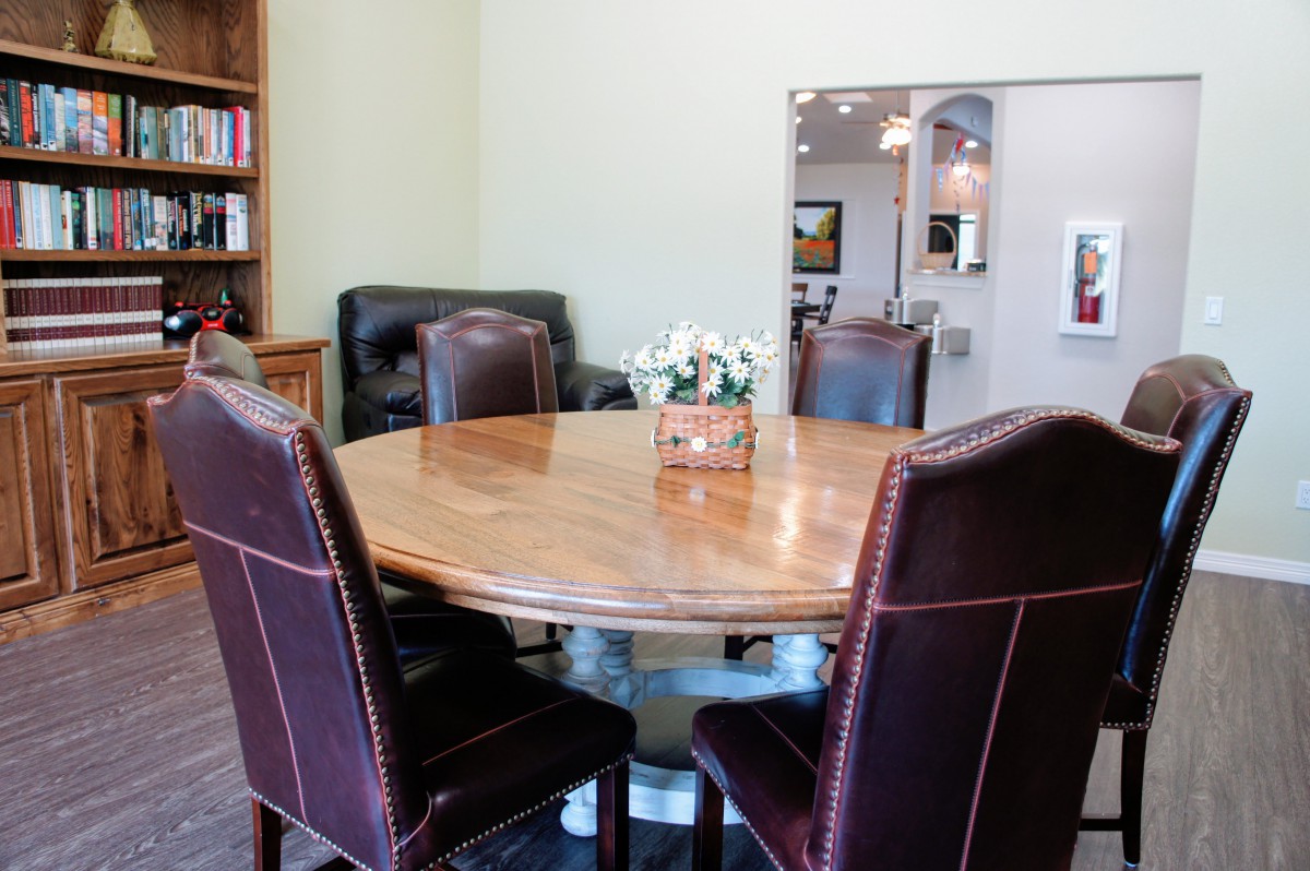 A conference room with a round wooden table and leather chairs, accompanied by a bookcase.