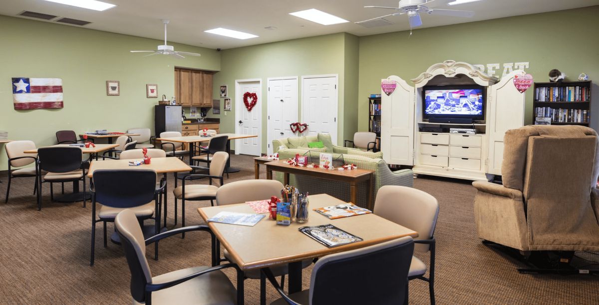A cozy community room with tables and chairs, a kitchenette, festive decorations, and a television.