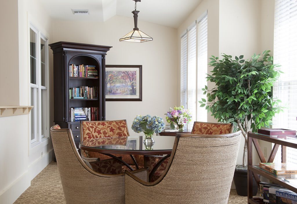A cozy dining room with a round table, modern chairs, a bookshelf, and decorative elements like plants and artwork.
