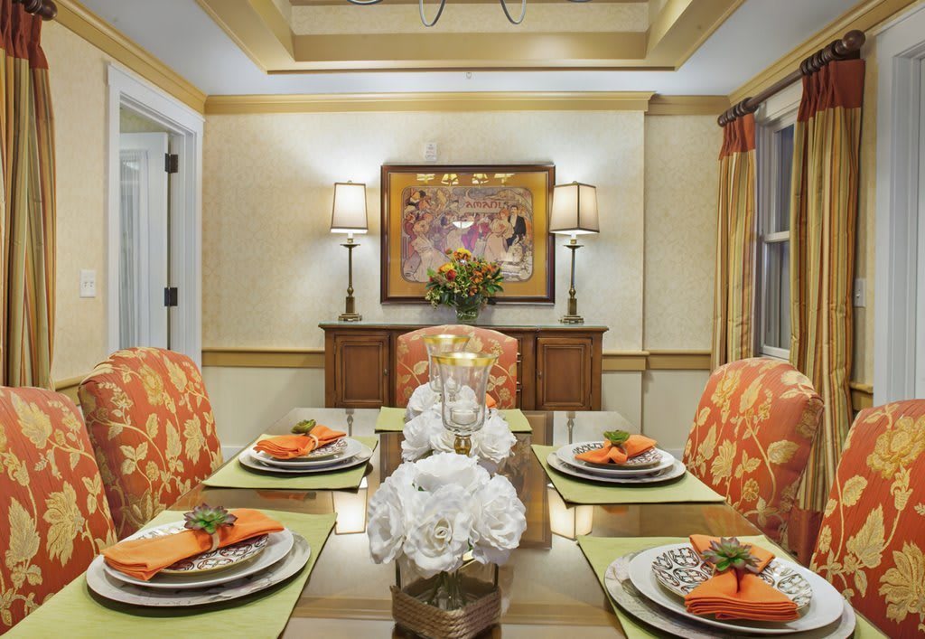 A beautifully decorated dining room with orange accents, elegant floral arrangements, and soft lighting.