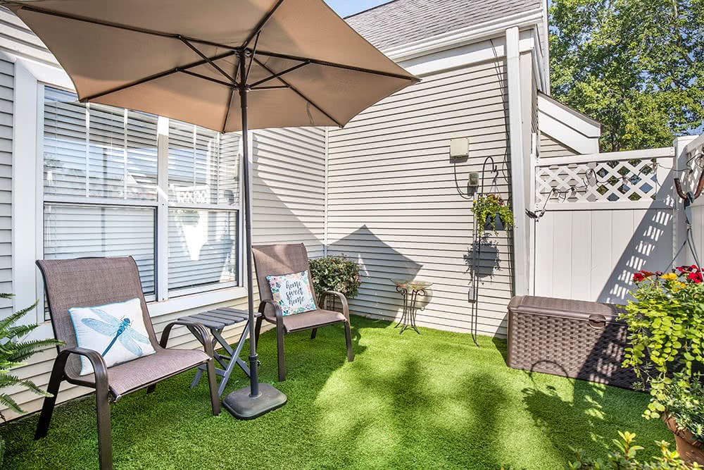 A cozy patio setup with chairs and an umbrella on a green lawn.