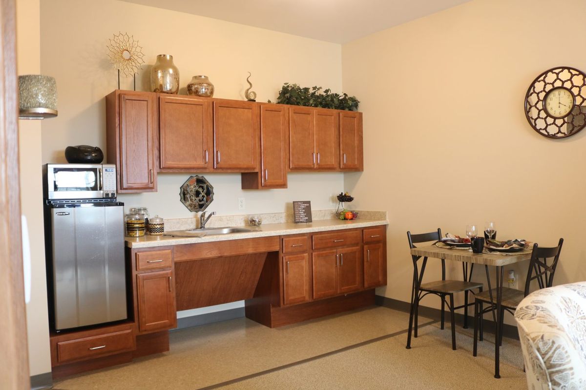 A modest kitchen area featuring wooden cabinets, countertops with decor, a small table and chairs, and kitchen appliances.