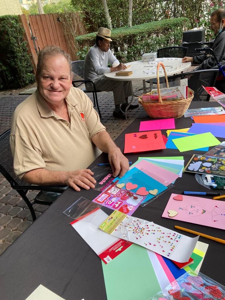 A man sitting at an outdoor table with colorful crafting supplies and smiling.