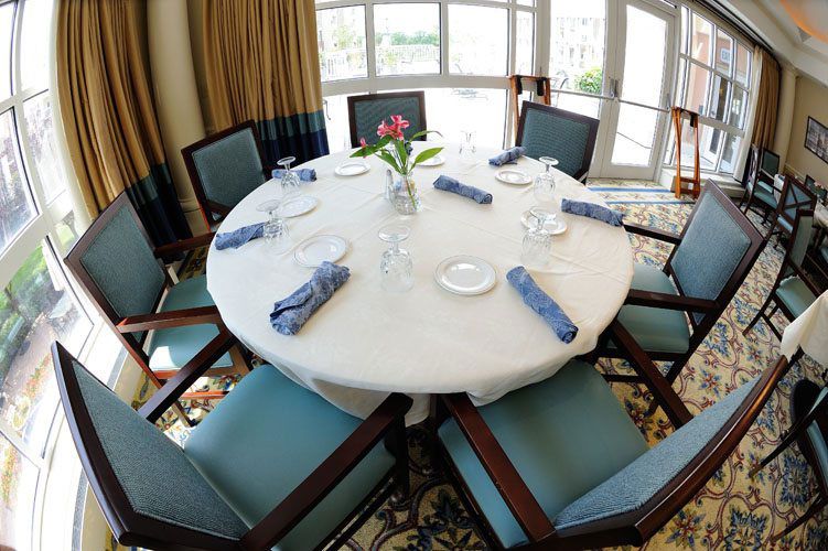 A beautifully set round dining table with six chairs, featuring blue napkins, glasses, and a vase of flowers at the center.