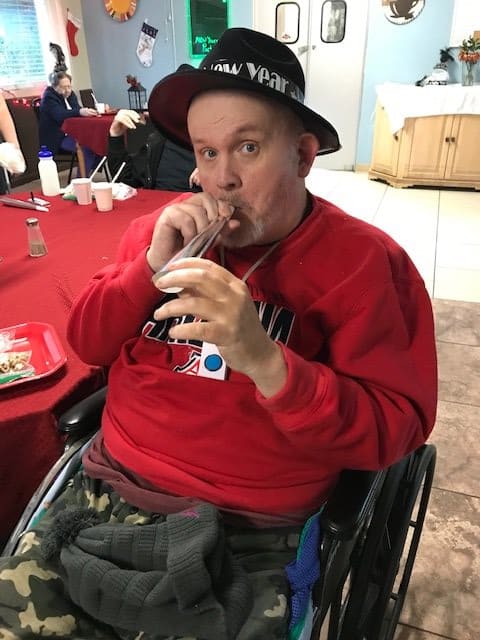 A man in a wheelchair wearing a hat and sipping a drink through a straw indoors.