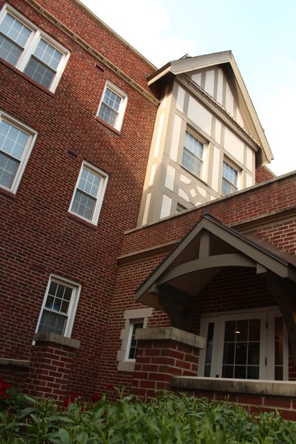 An exterior view of a brick residential building with multiple windows and a gabled entrance.
