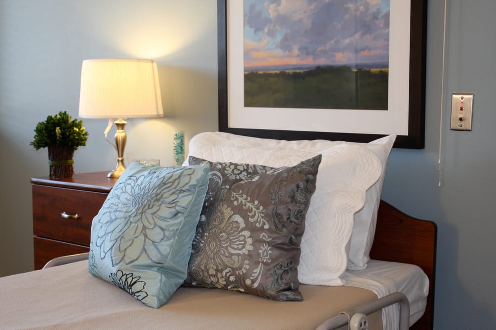 A cozy bedroom setup featuring decorative pillows, a bedside lamp, and a framed painting above the bed.