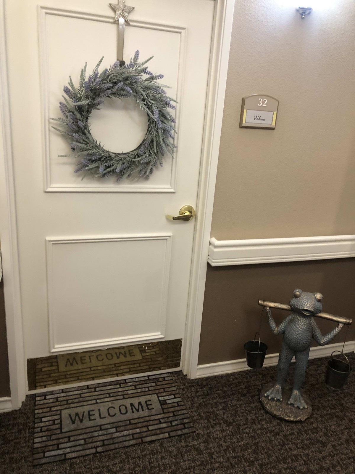 A decorated door with a wreath and a frog statue in the hallway.