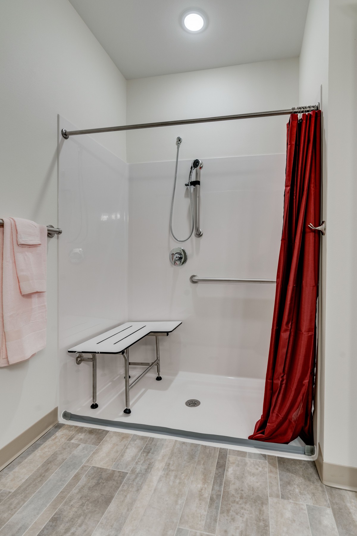 An accessible shower setup with a folding bench, handheld showerhead, grab bar, and red curtain.