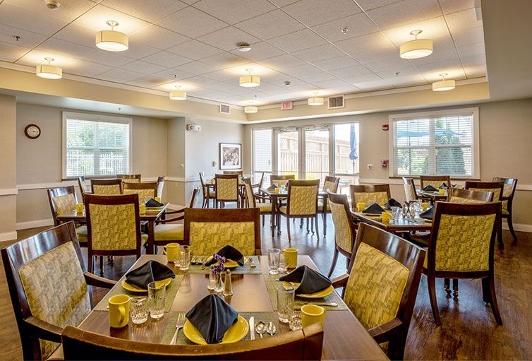An elegant dining room featuring neatly arranged tables with stylish place settings, complemented by large windows providing natural light.