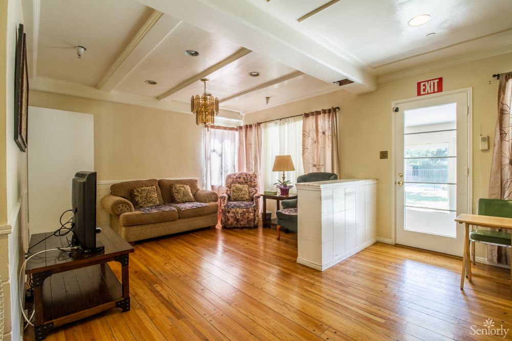 A cozy living room with hardwood flooring, featuring a sofa, armchair, lamp, and chandelier.