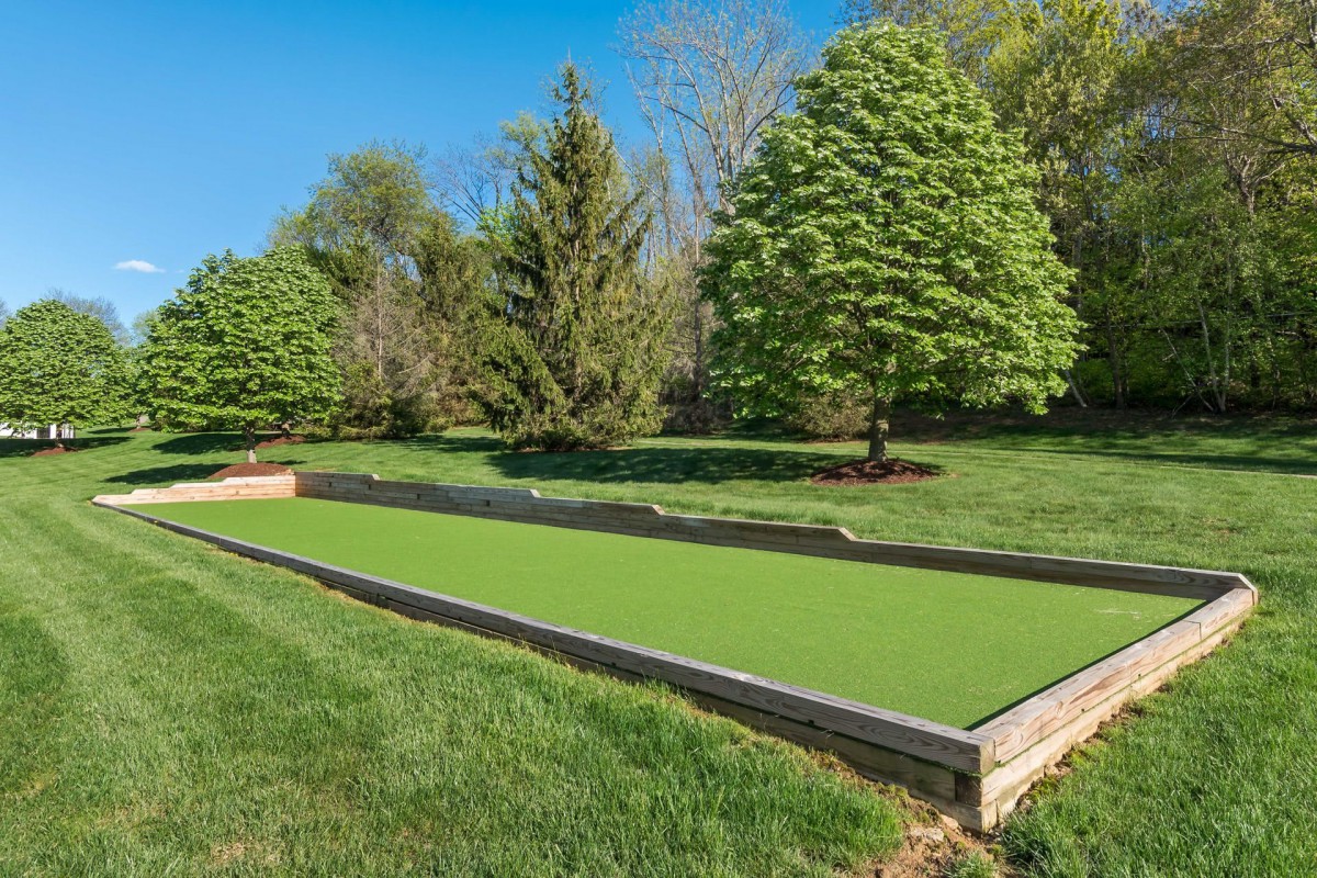 A well-maintained bocce court surrounded by lush greenery and trees on a sunny day.