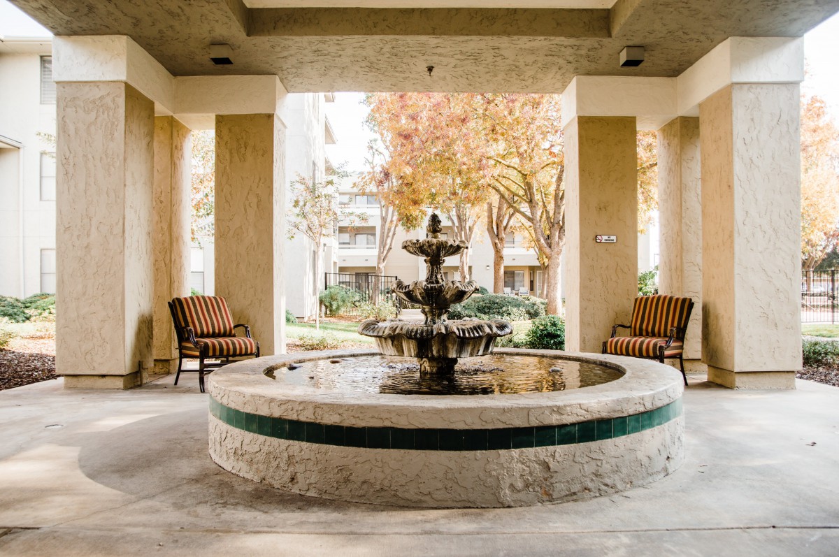 A serene indoor courtyard featuring a central fountain surrounded by chairs, with autumn trees visible in the background.