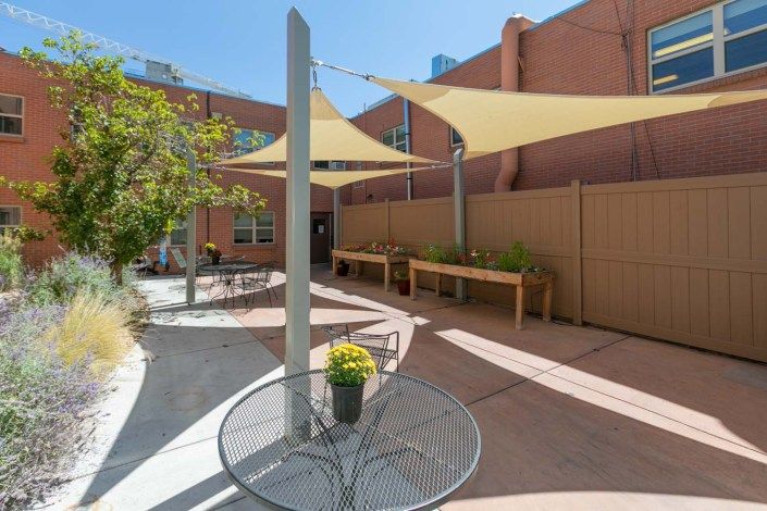 A modern outdoor patio with shade sails, tables, chairs, and potted plants.