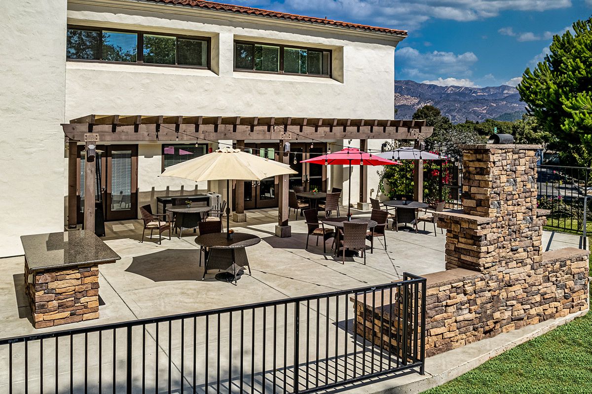 A modern outdoor patio area with tables, chairs, and umbrellas under a clear blue sky.