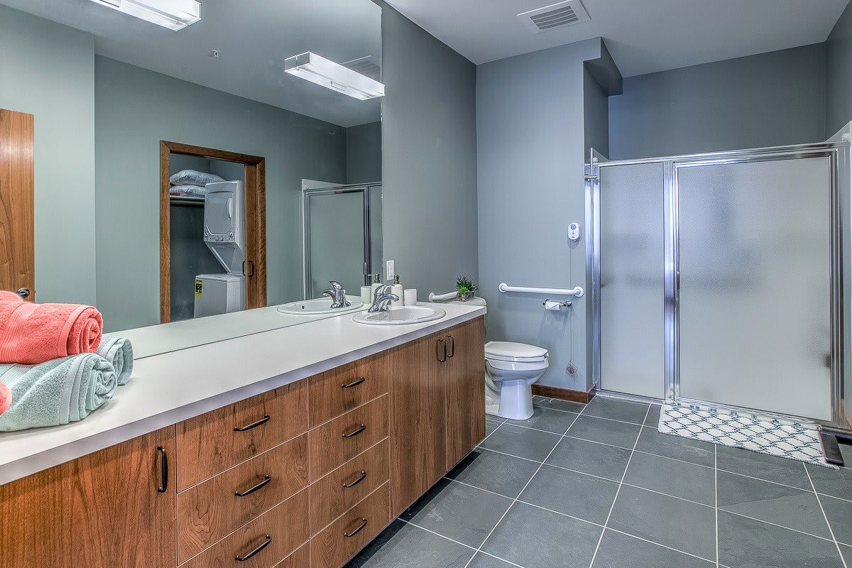 A modern bathroom featuring a wooden vanity with a large mirror, a toilet, and a spacious shower area.