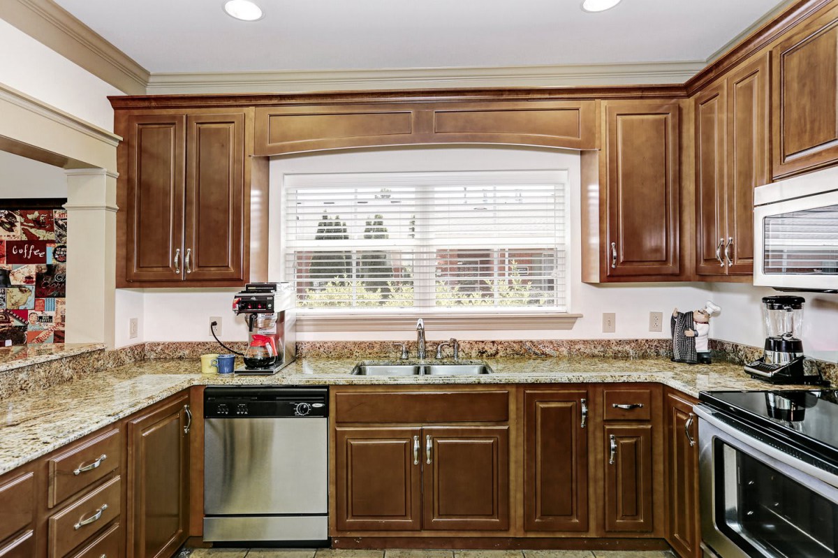 A spacious kitchen with wooden cabinetry, featuring a sink beneath a large window and modern appliances on the countertop.