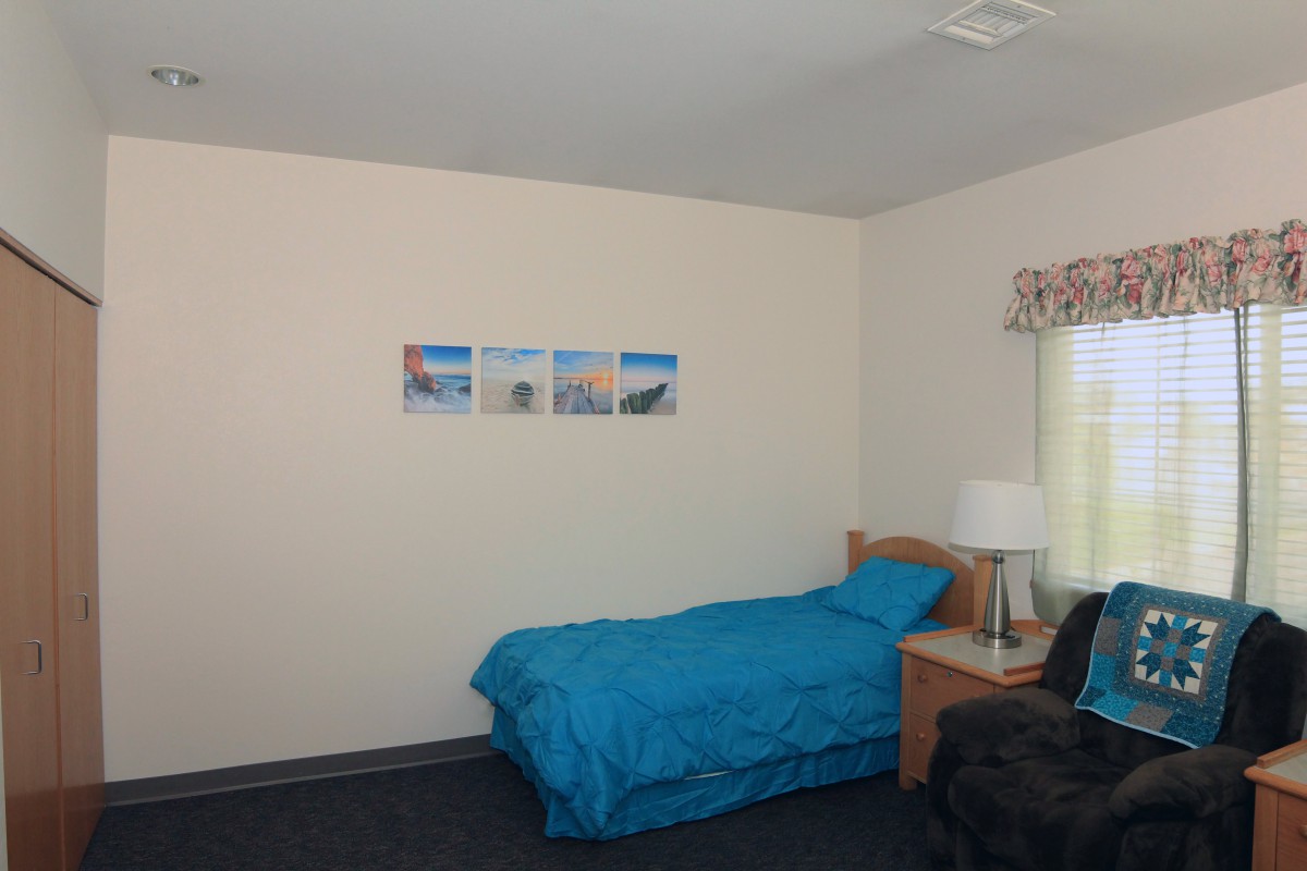 A simple bedroom with a single bed and blue bedding, featuring a nightstand and wall art.