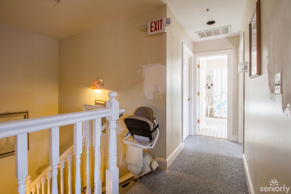 A hallway with a stair lift and an exit sign on the wall.