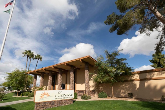 A sunny day view of a building with a sign, surrounded by trees and under a partly cloudy sky.