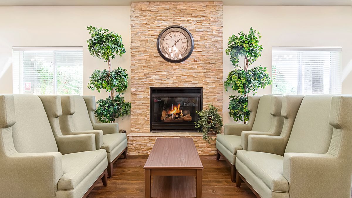Cozy living room with a fireplace, surrounded by armchairs and indoor plants.