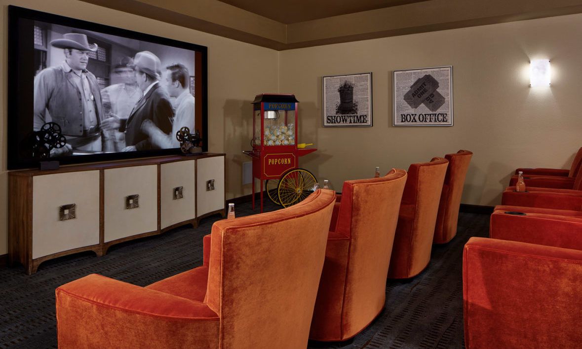 A cozy home theater with orange seats, a large movie screen, and a popcorn machine.