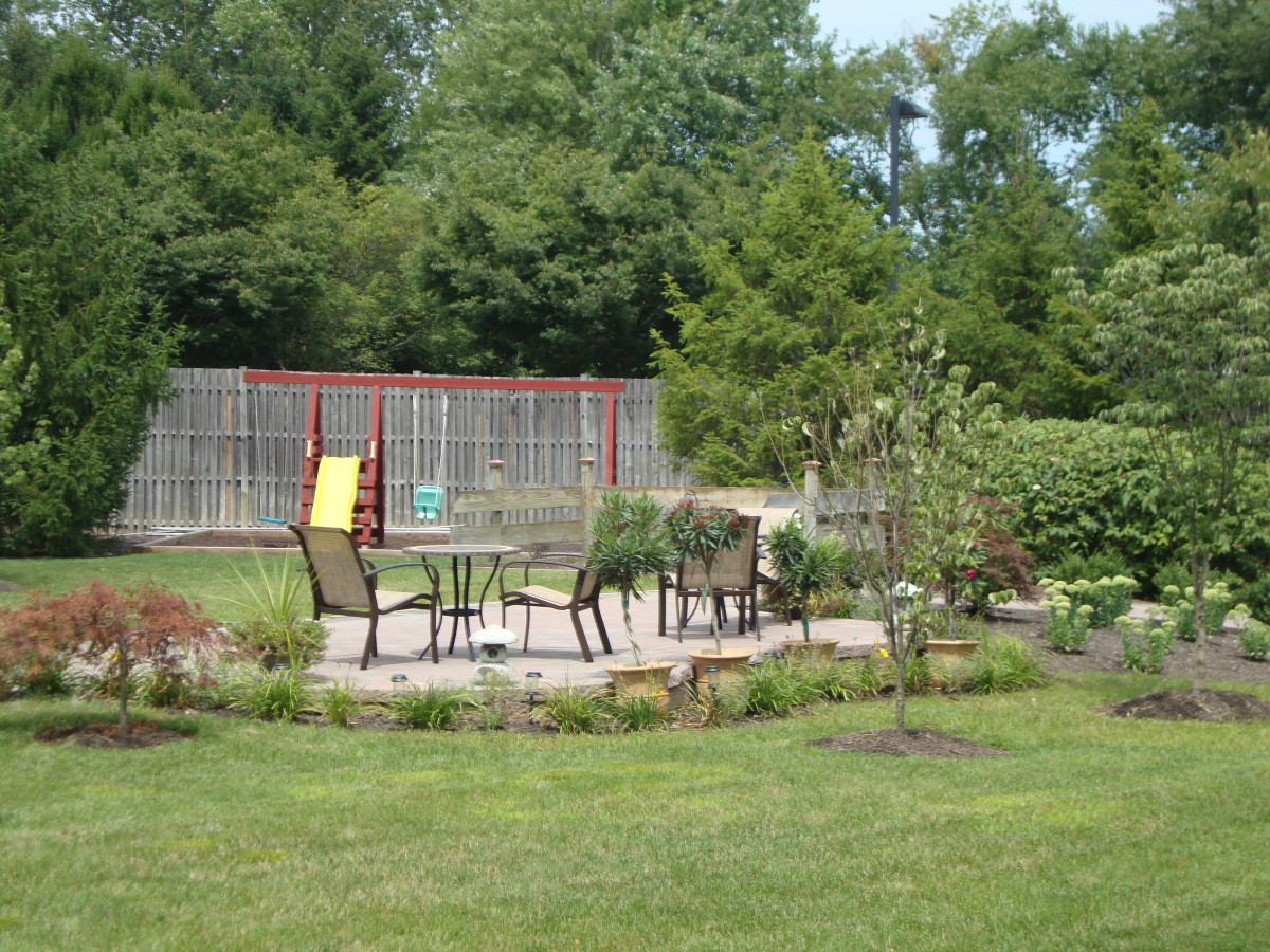 A serene garden patio with outdoor furniture surrounded by lush greenery and trees.