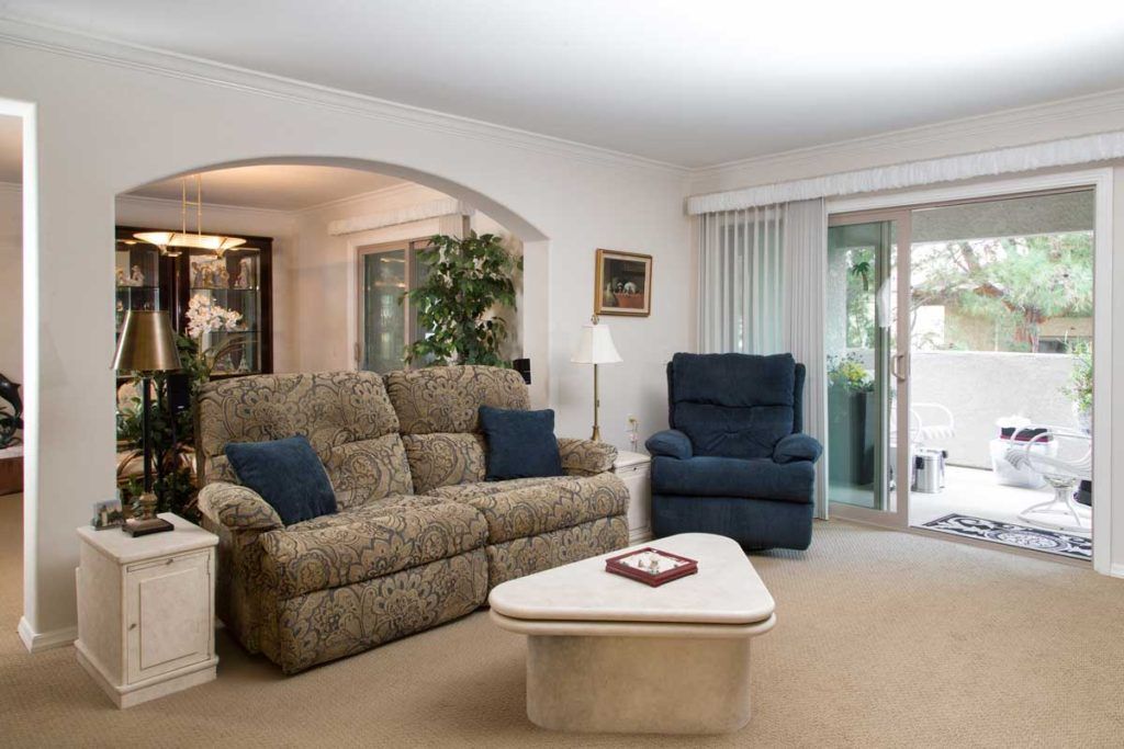 A cozy living room with a sofa, armchair, and coffee table, featuring indoor plants and decor.