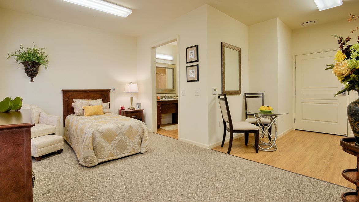A cozy bedroom with a neatly made bed, desk, and chair, featuring warm lighting and elegant decor.