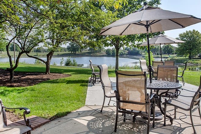 A scenic outdoor patio with tables and umbrellas overlooking a tranquil lake.