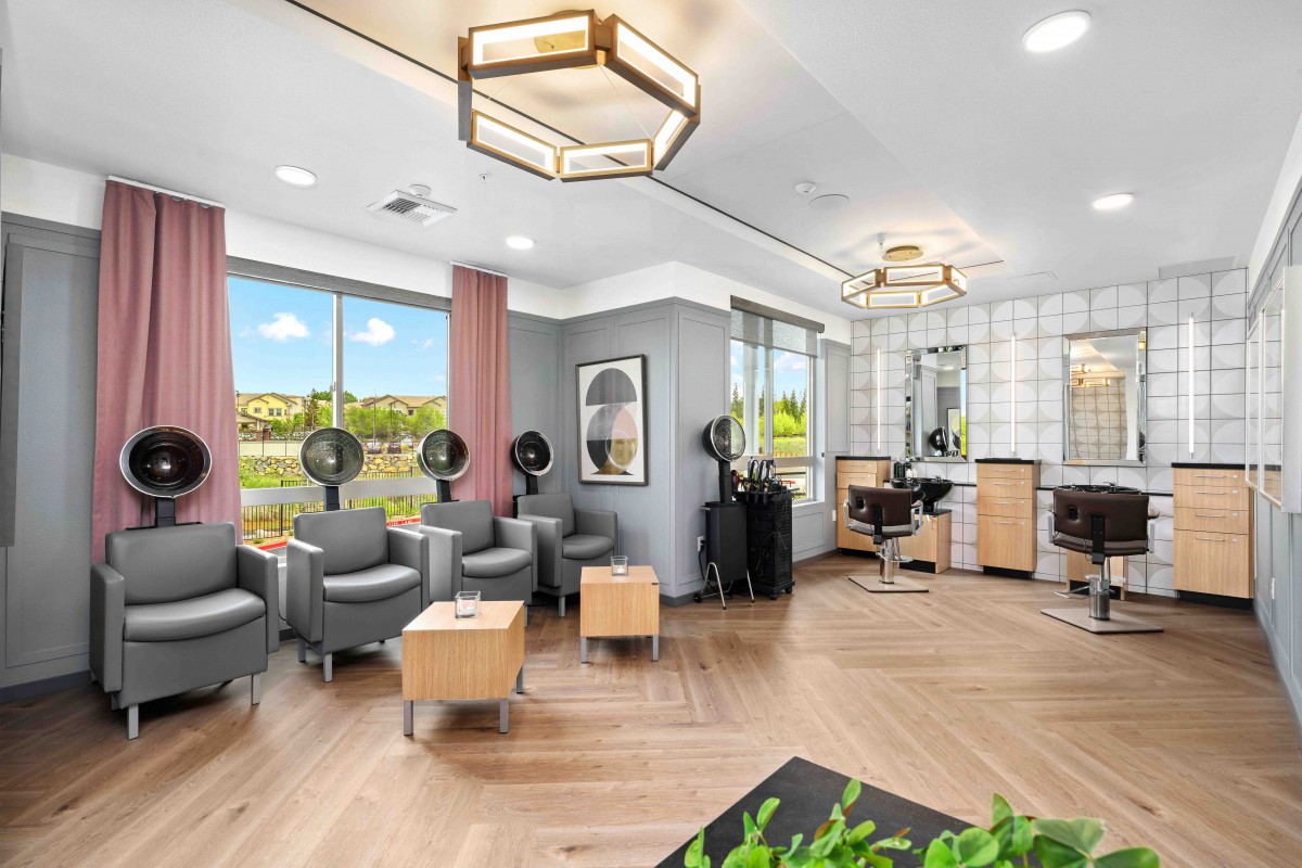 A modern salon interior featuring seating with hair dryers, stylish lighting fixtures, and large windows.