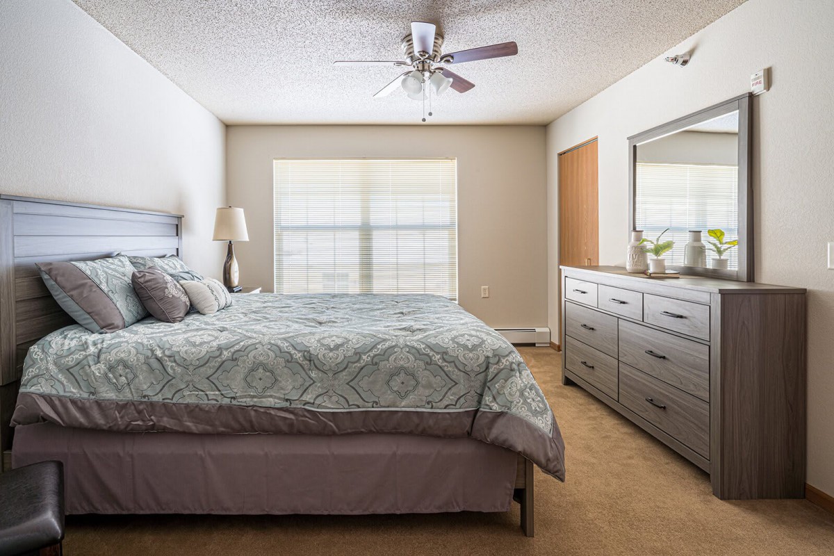 A cozy and neatly arranged bedroom with a large bed, dresser, and ceiling fan.