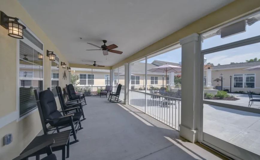 A spacious porch with rocking chairs and ceiling fans, overlooking a sunny patio.