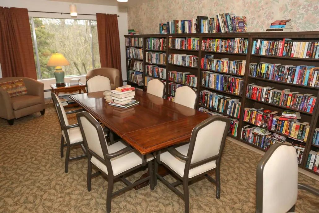 A cozy library room with a wooden table surrounded by chairs and bookshelves filled with books.