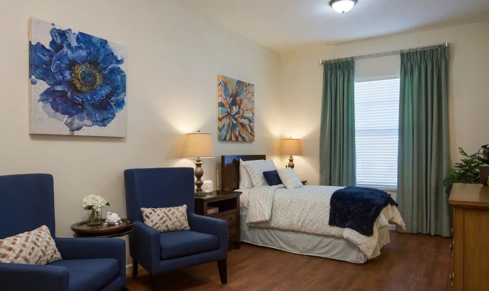 A cozy bedroom with a neatly made bed, two armchairs, and decorative artwork on the walls.