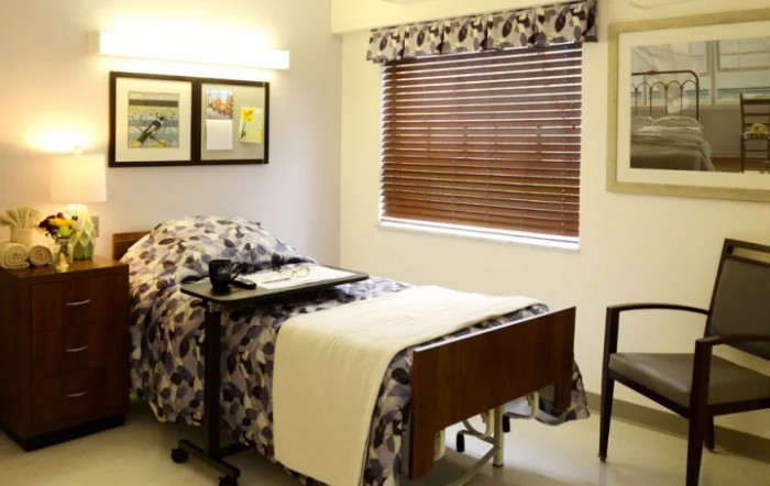 A hospital room featuring a bed, window with blinds, and framed pictures on the wall.