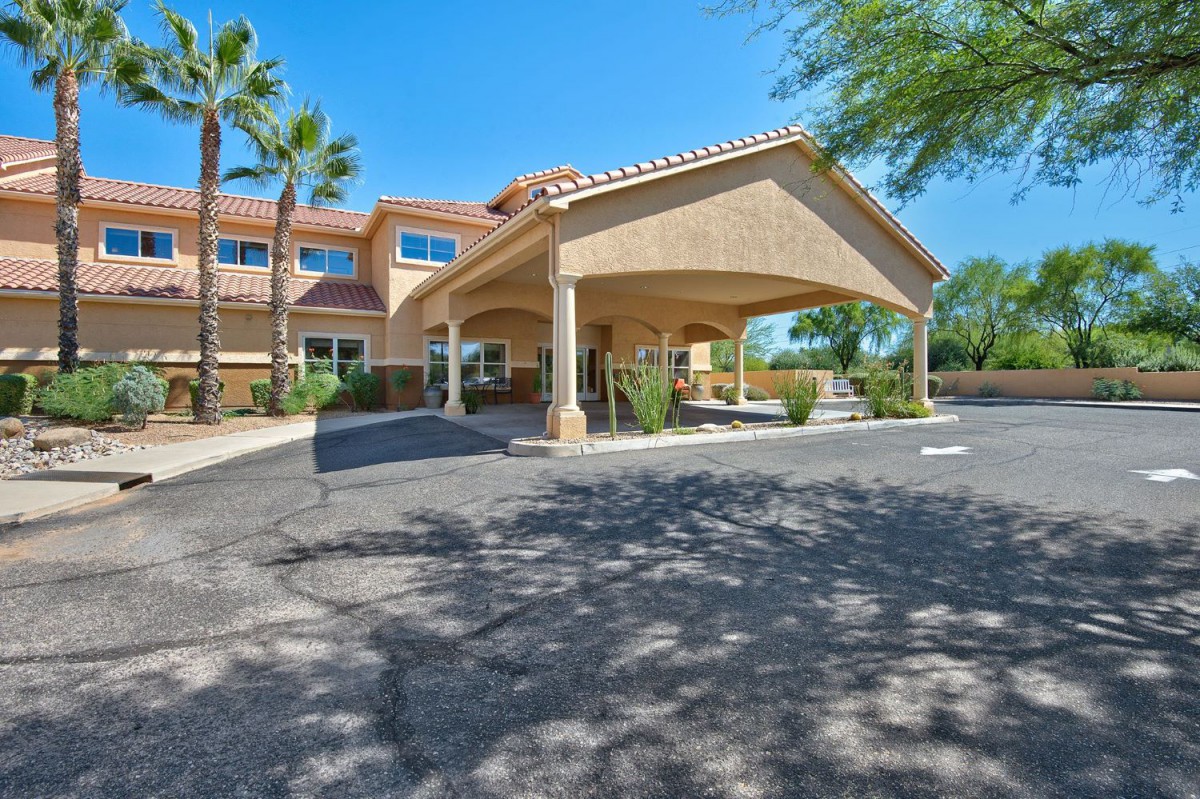 A sunny day view of a building with a covered entrance surrounded by palm trees.