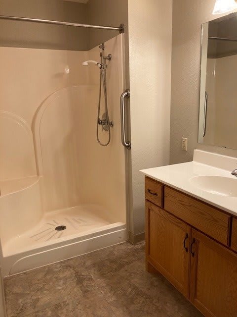 A modern bathroom with a shower, sink, and wooden cabinet.