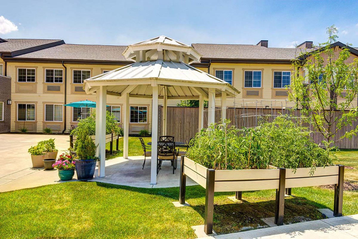 A charming gazebo surrounded by greenery in a garden setting, with a building visible in the background.