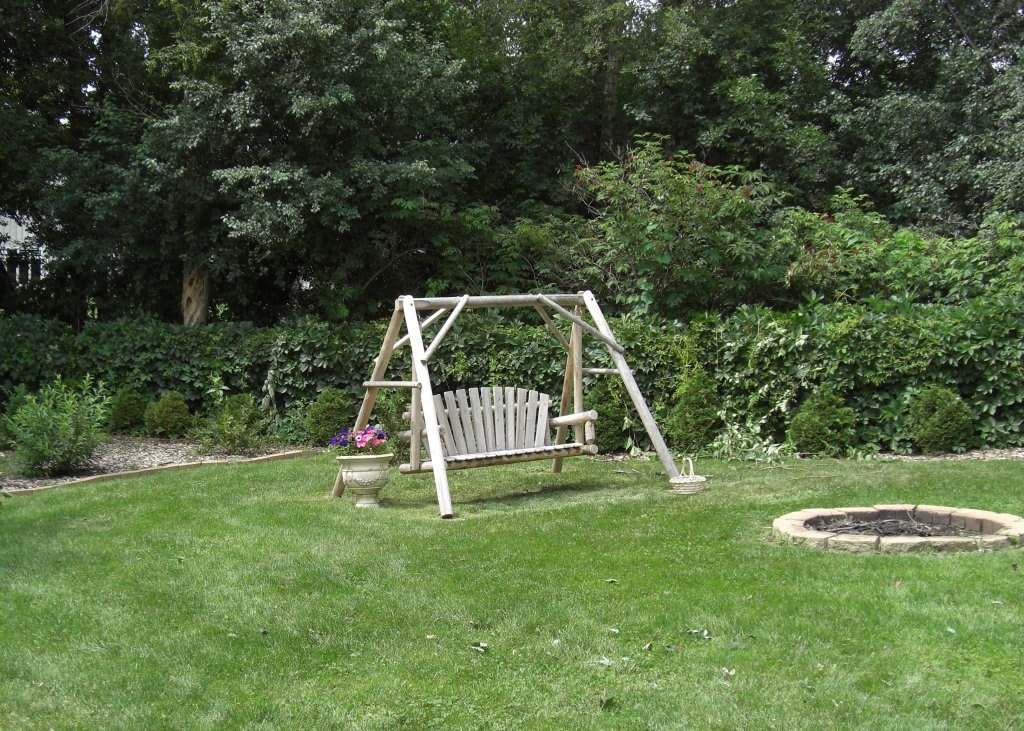 A peaceful garden scene featuring a bench swing set amidst a lush green lawn and surrounded by trees.